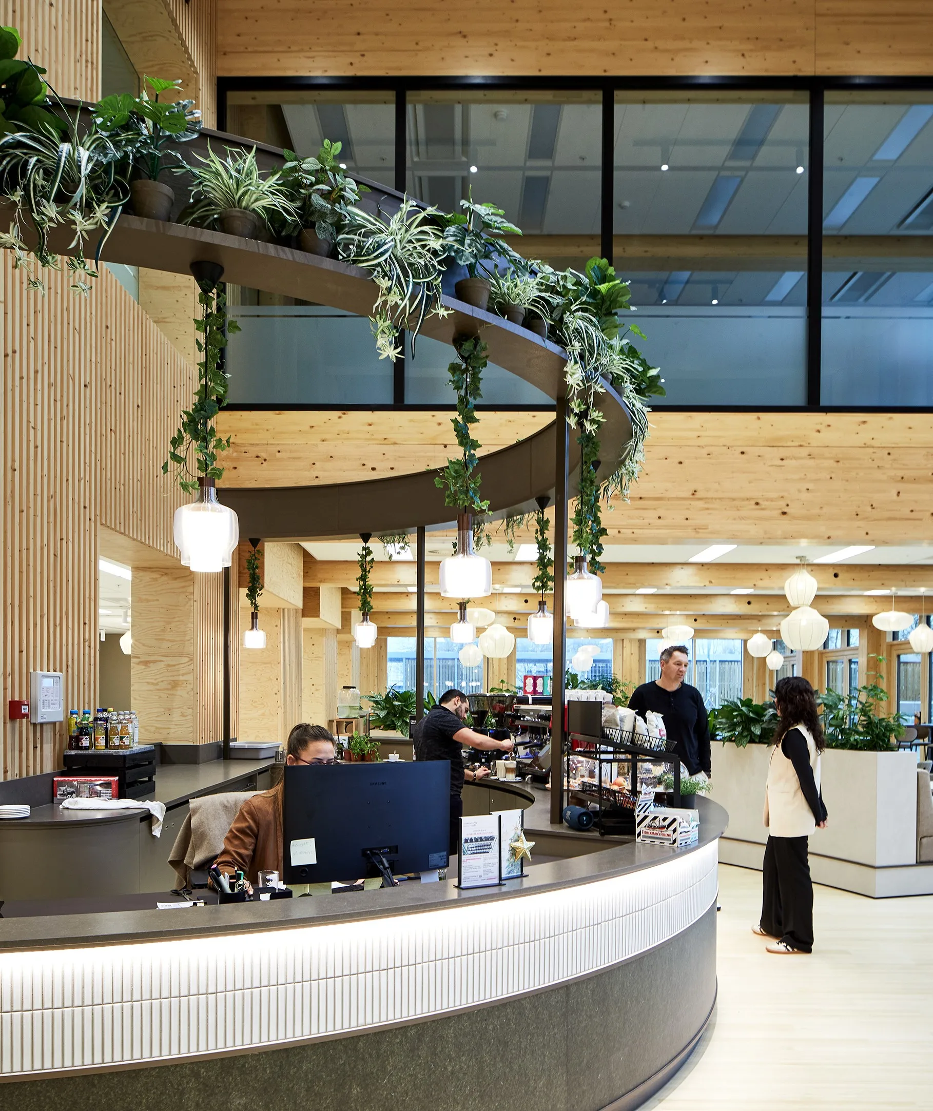 Een moderne receptie met planten en houten interieur, waar een medewerker achter een bureau zit en klanten worden geholpen.