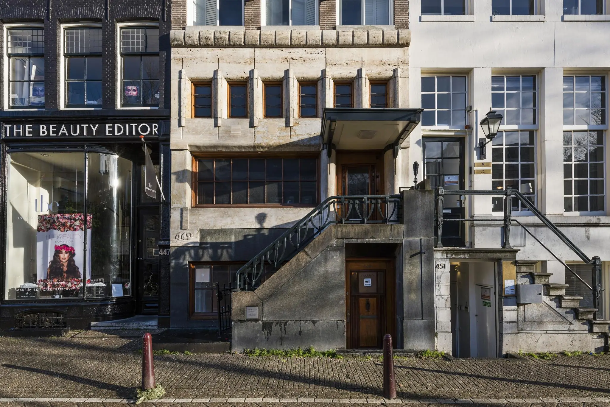 Gevels van drie panden aan de Herengracht in Amsterdam met huisnummers 447, 449 en 451, waaronder een beautysalon en een entree met trap.