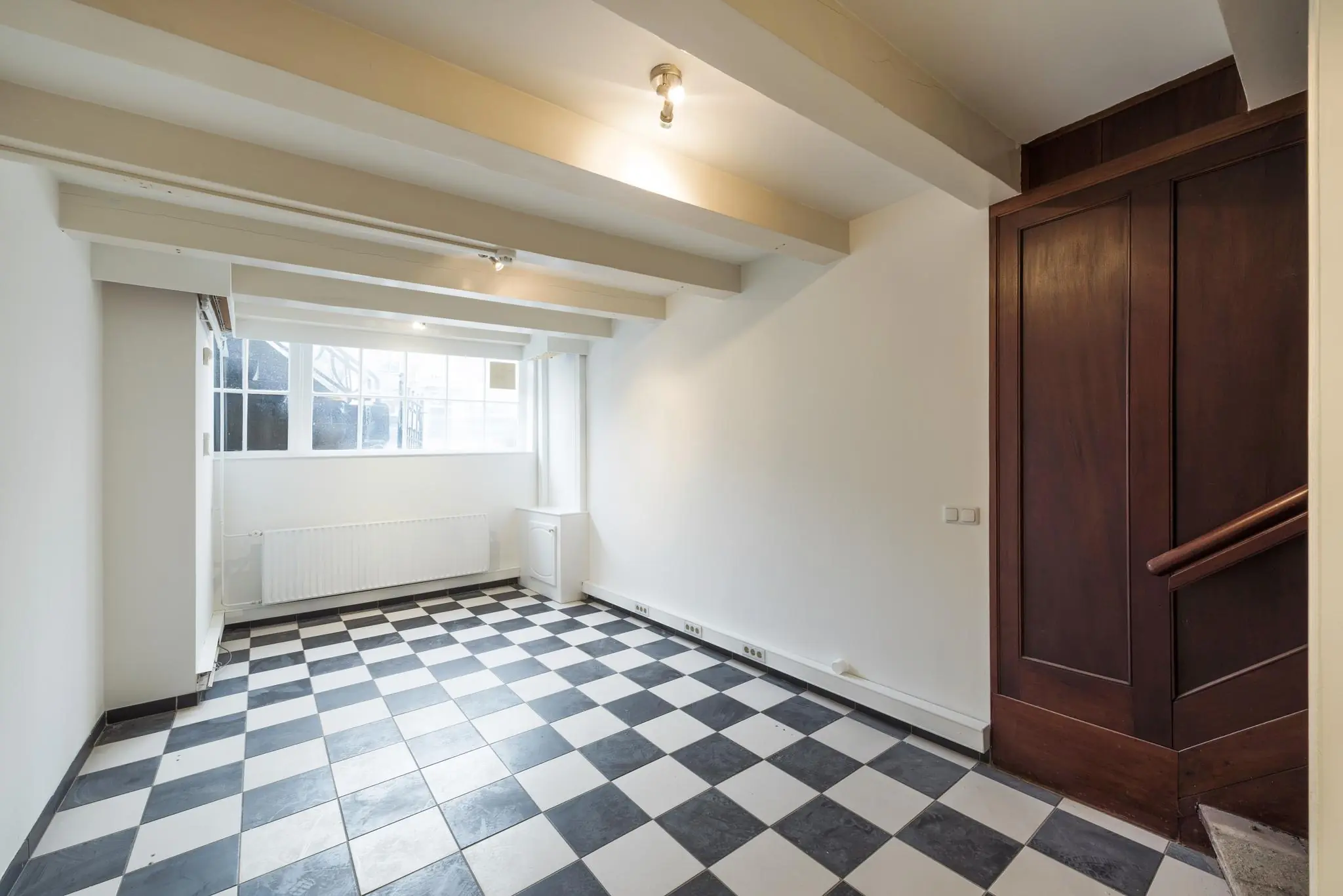 Kamer met zwart-wit geblokte tegelvloer, houten trapkast en groot raam aan de Herengracht.