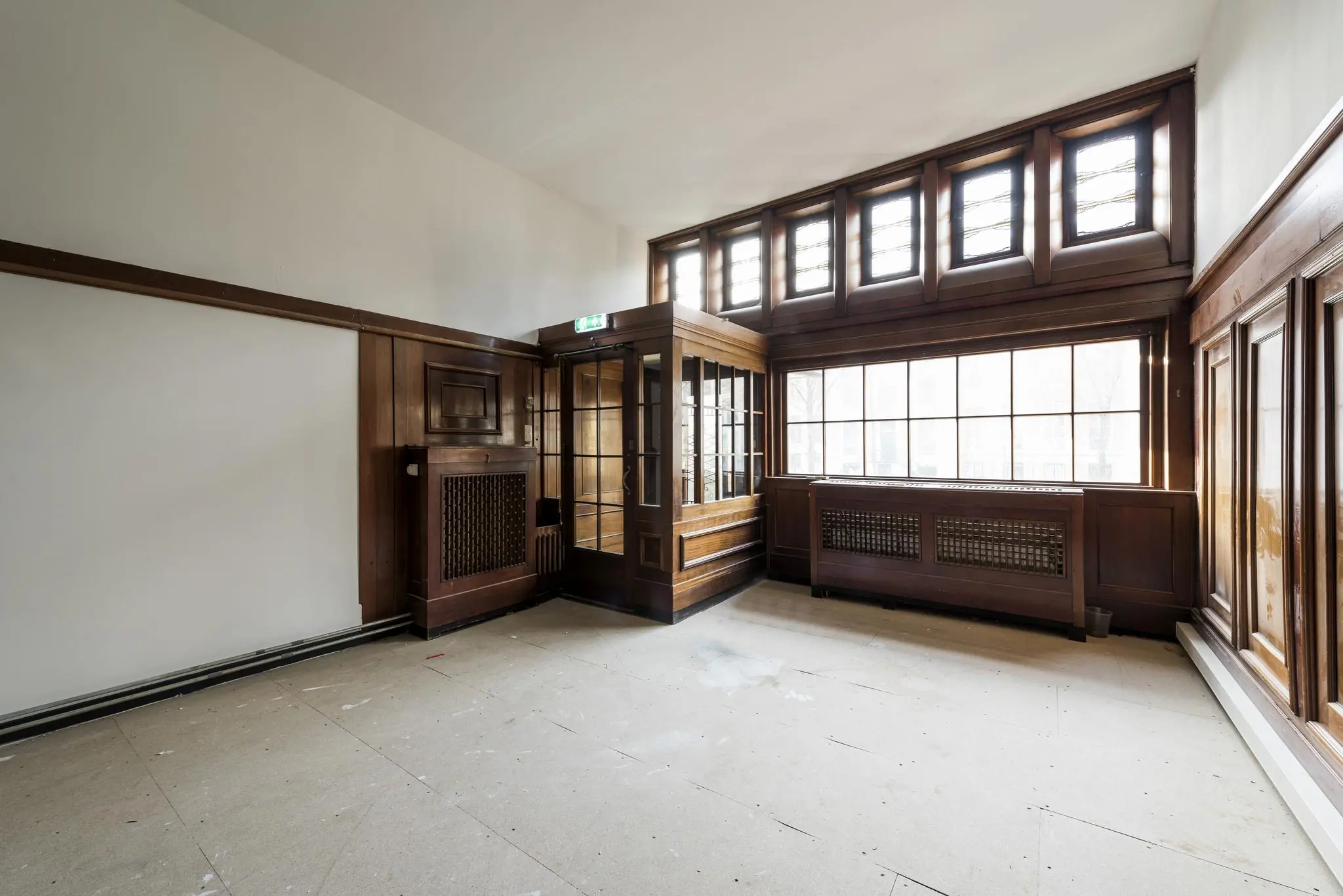 Leegstaand en licht kantoorinterieur aan de Herengracht met karakteristieke houten lambrisering en grote ramen.