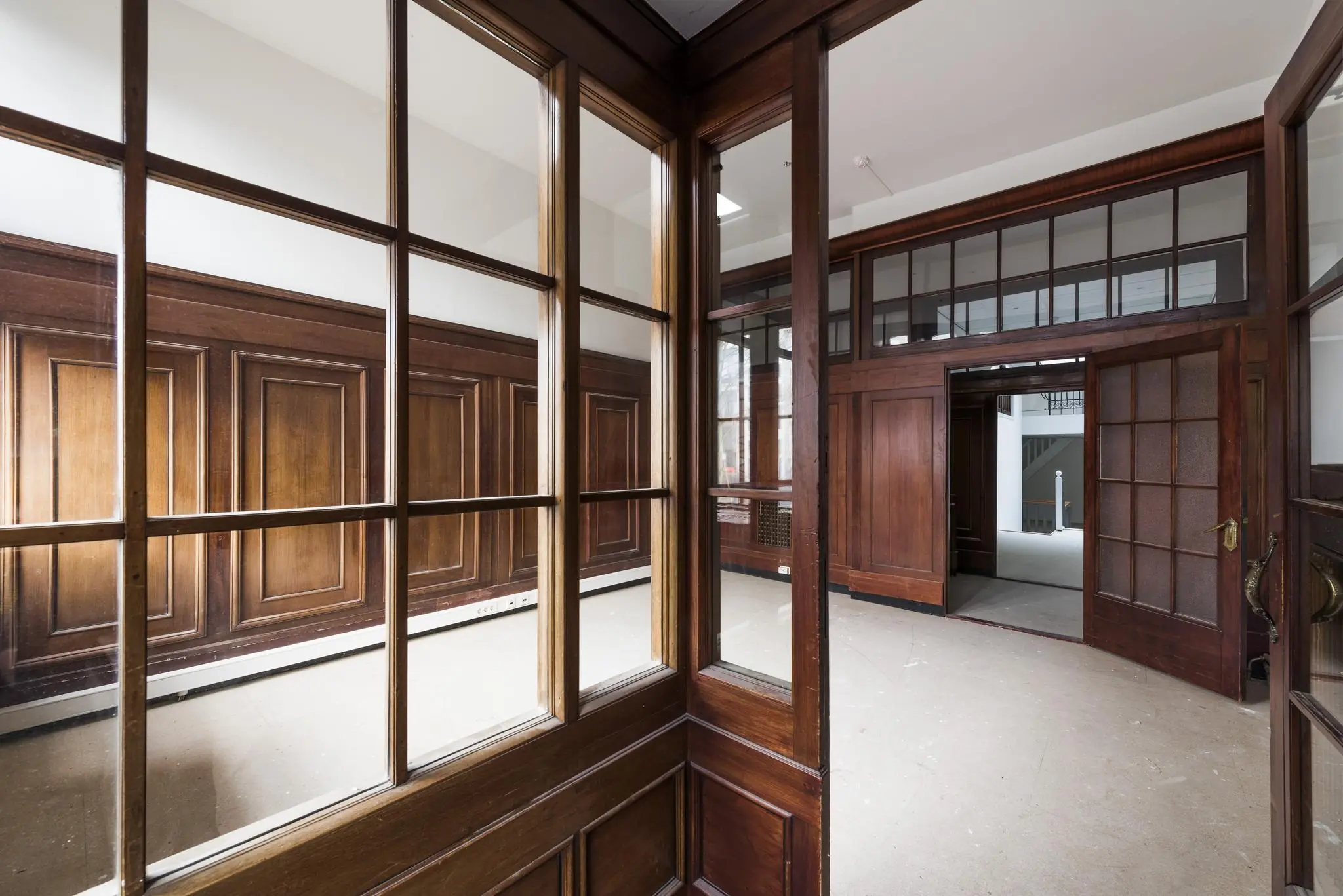 Interieur van een leegstaand pand aan de Herengracht met houten lambrisering, glas-in-looddeuren en grote raampartijen.