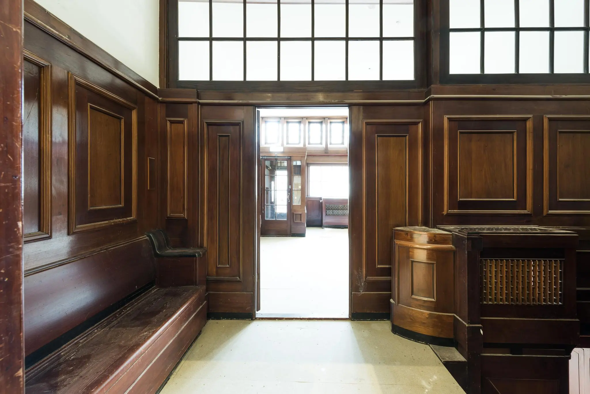 Doorkijk naar een lichte ruimte vanuit een hal met klassieke houten wandpanelen en ingebouwde bank in een interieur aan de Herengracht.