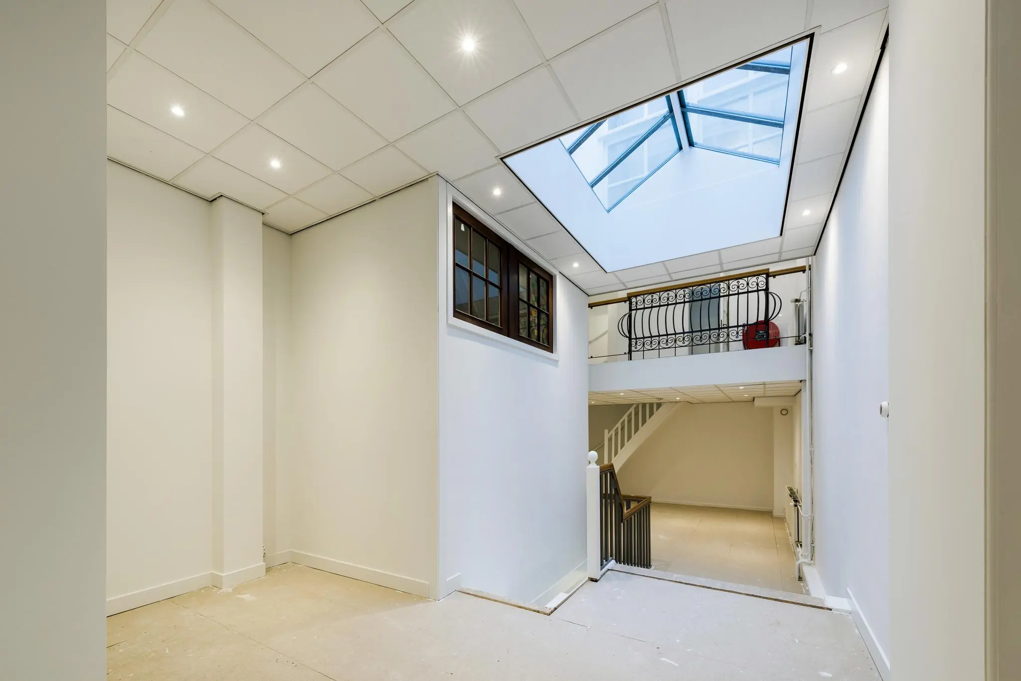 Lichte en moderne hal met trap, dakraam en sierlijk smeedijzeren balkon aan de Herengracht.