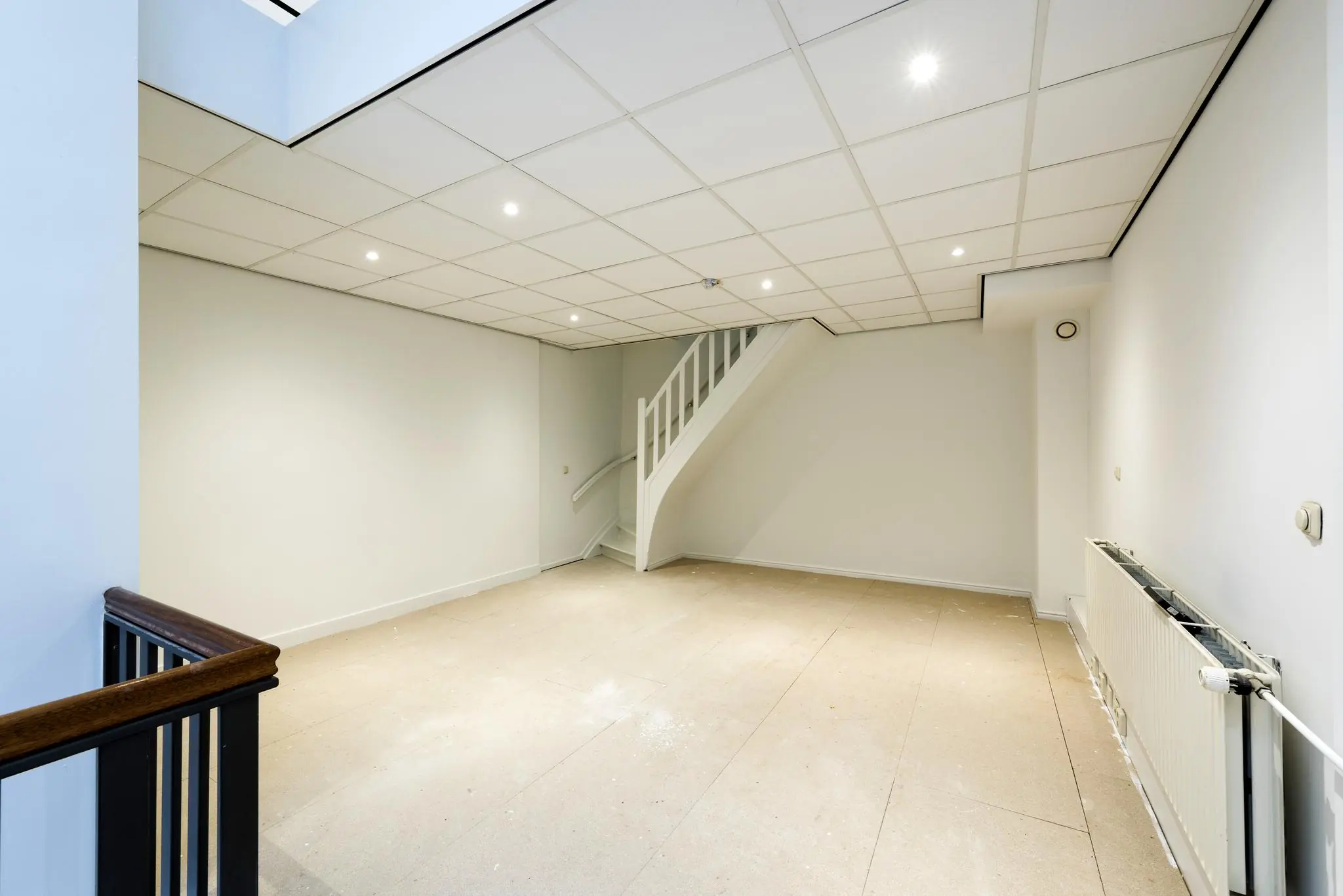 Lege kamer met trap, systeemplafond en radiator in pand aan de Herengracht.