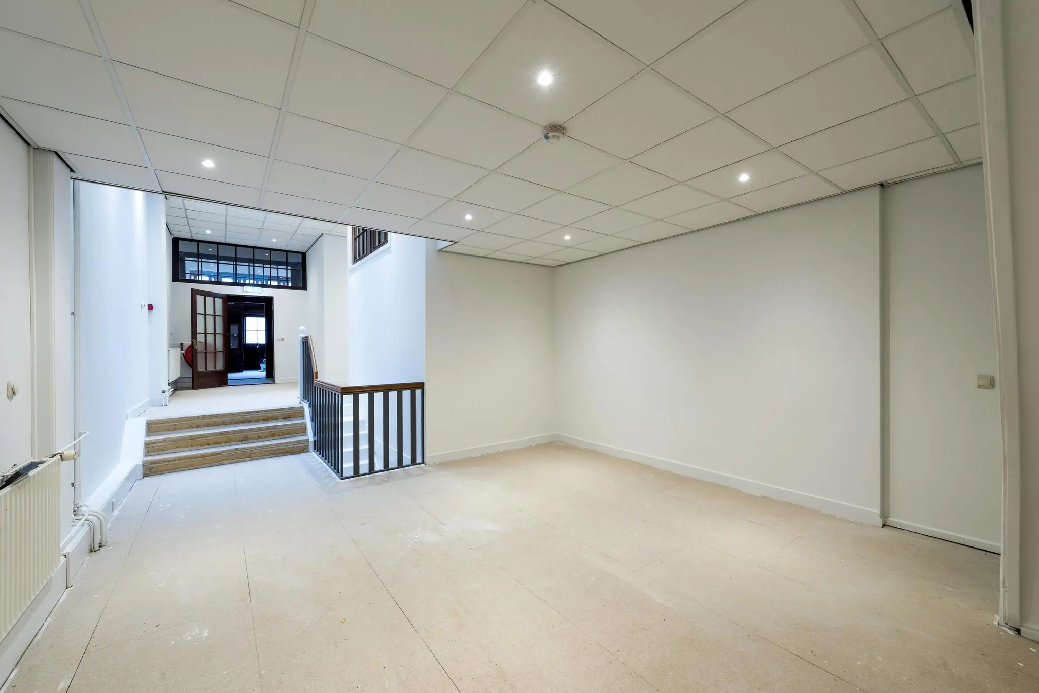 Leeg, witgeschilderd interieur met systeemplafond en trap in een pand aan de Herengracht.