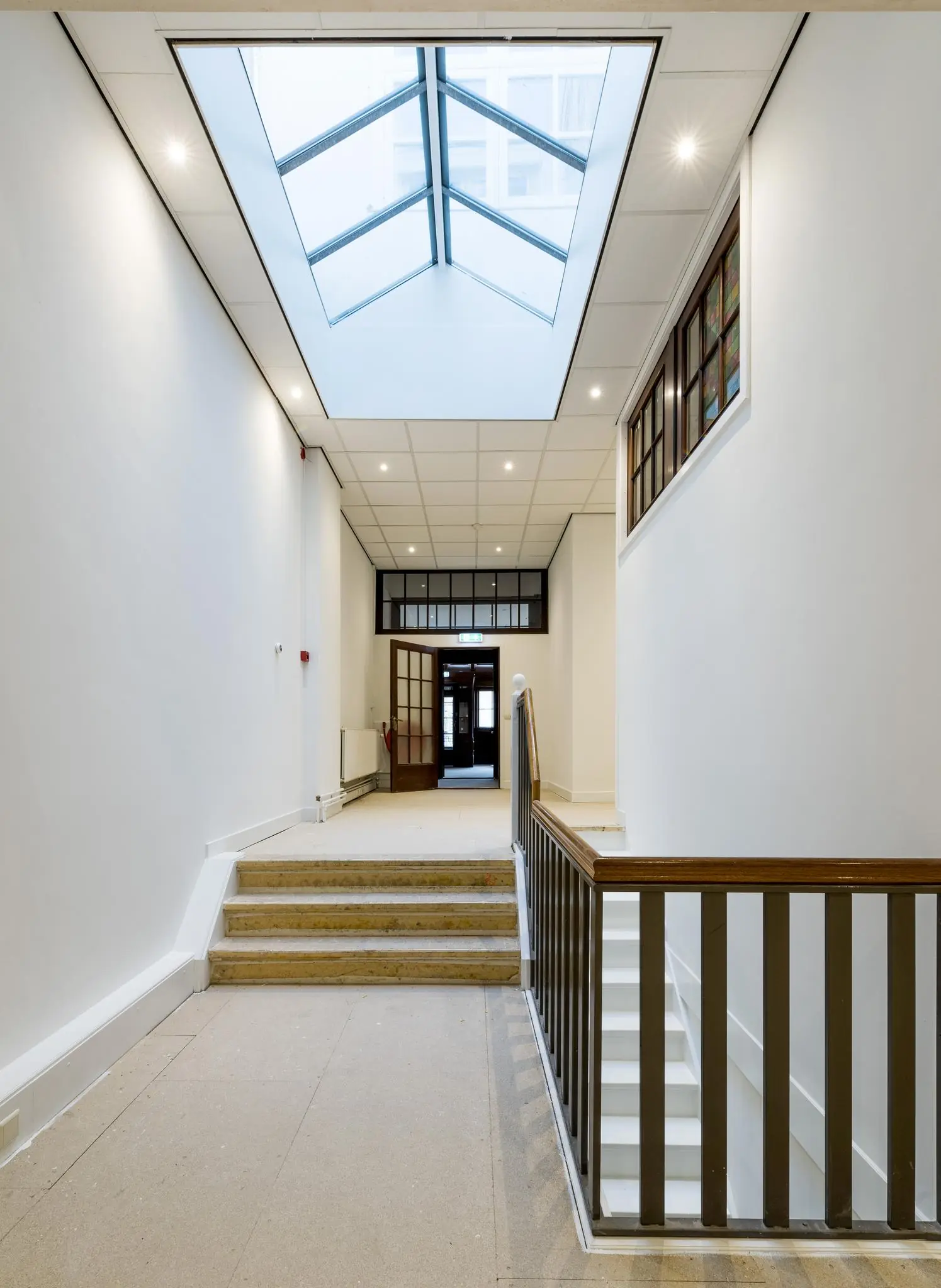 Heldere, moderne gang in een pand aan de Herengracht met een glazen dakraam, trap en houten balustrade.