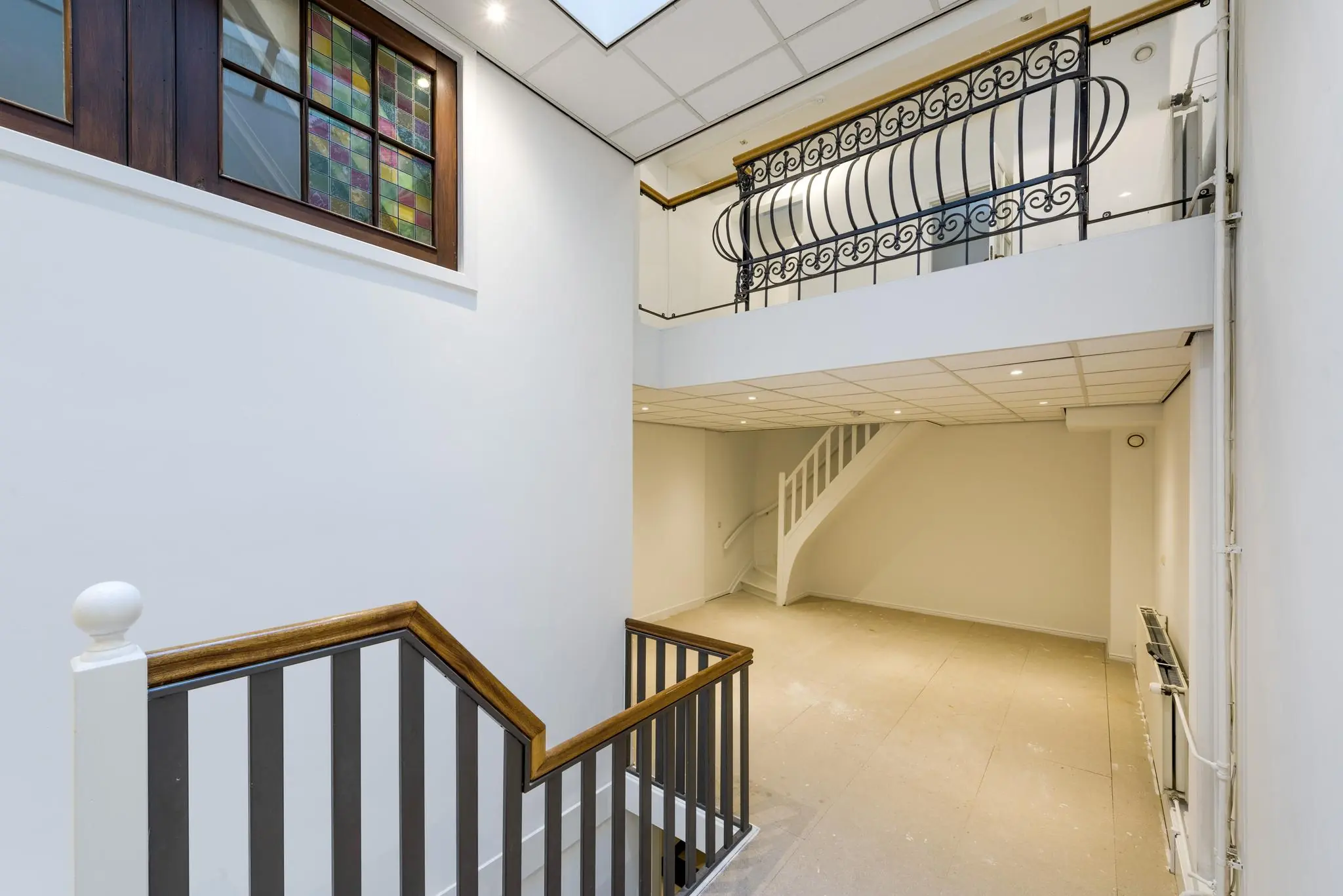 Opknapruimte aan de Herengracht met split-level indeling, houten trap, sierlijk balkonhek en glas-in-loodraam.