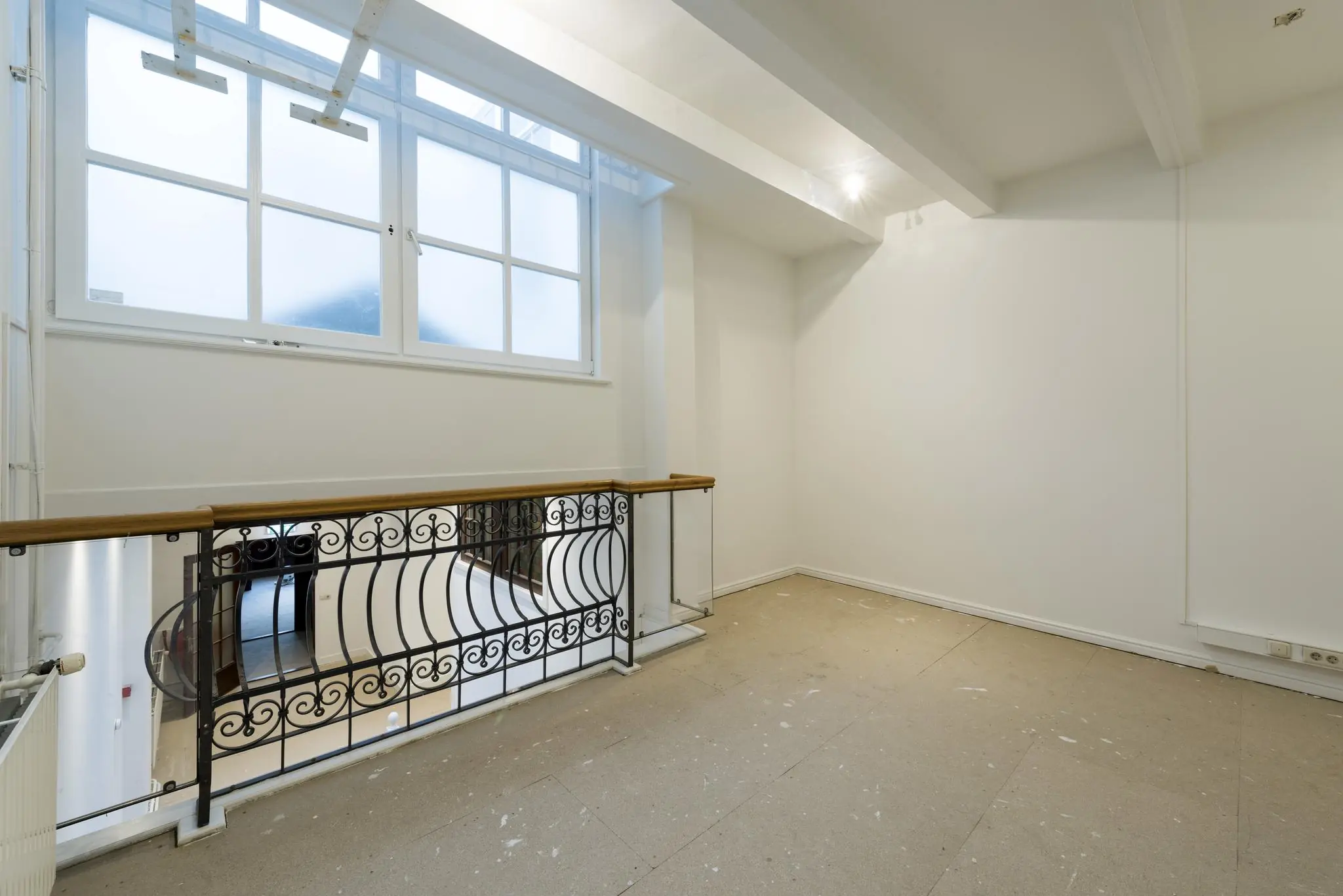 Leeg, witgeschilderd interieur met een groot matglas raam en sierlijk zwart smeedijzeren traphek aan de Herengracht.