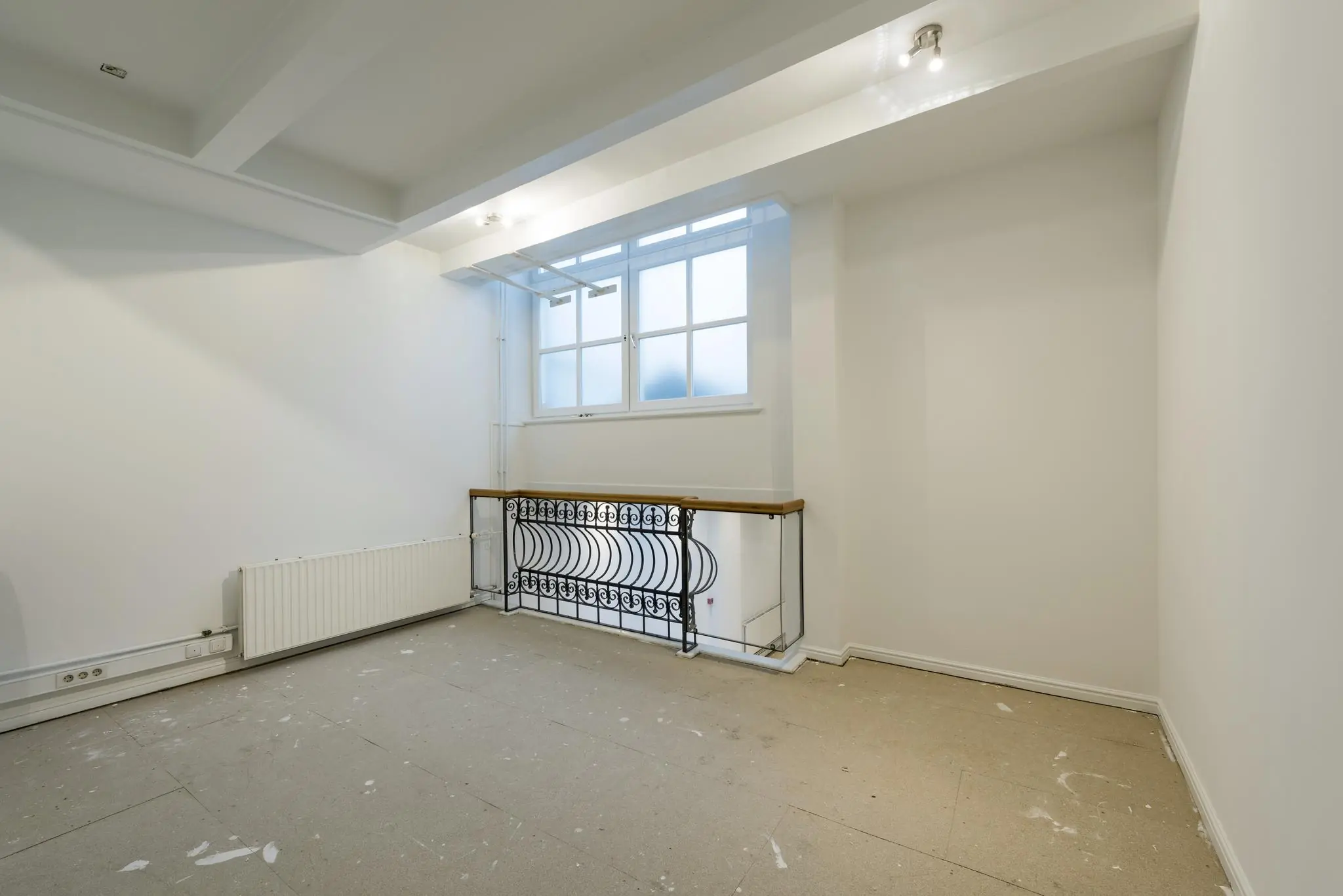 Lege, witte ruimte op Herengracht met groot raam, radiator en sierlijk smeedijzeren traphek.