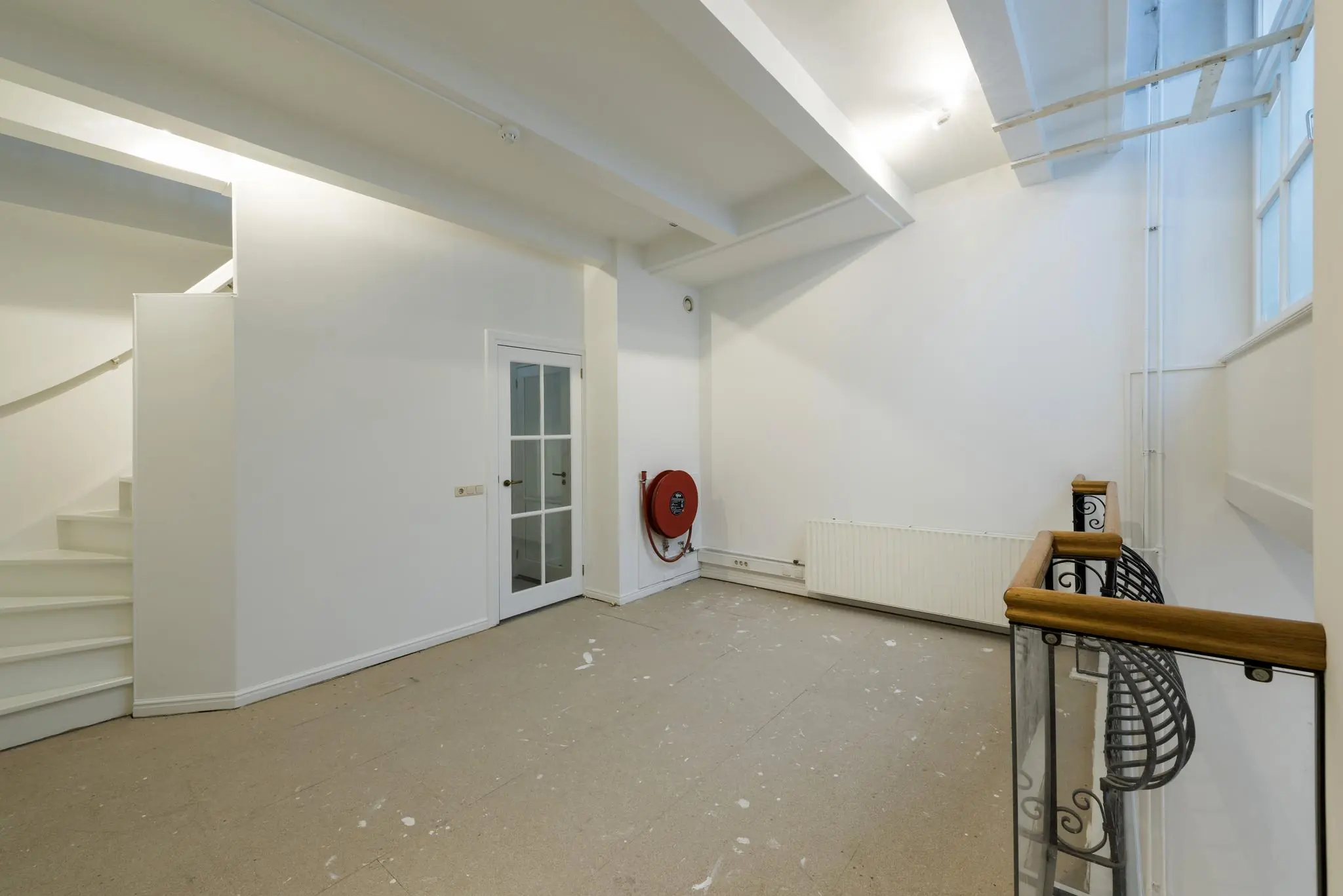 Lege witte ruimte met trap, glazen deur, brandslanghaspel en radiator in een pand aan de Herengracht.