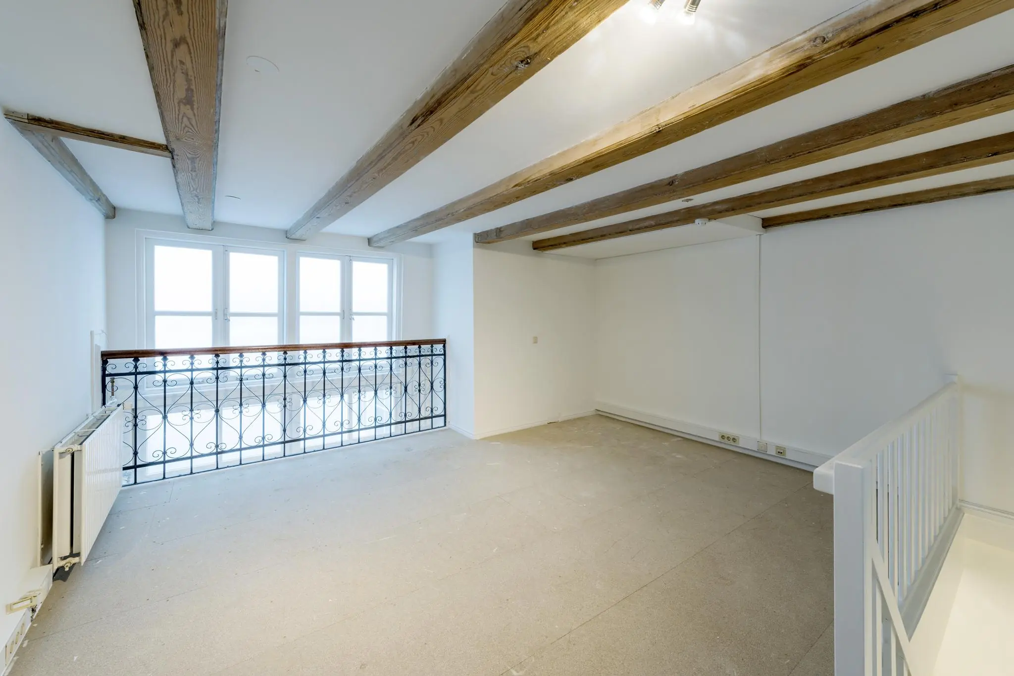 Lichte, lege zolderkamer aan de Herengracht met houten balken, gietijzeren balustrade en grote ramen.