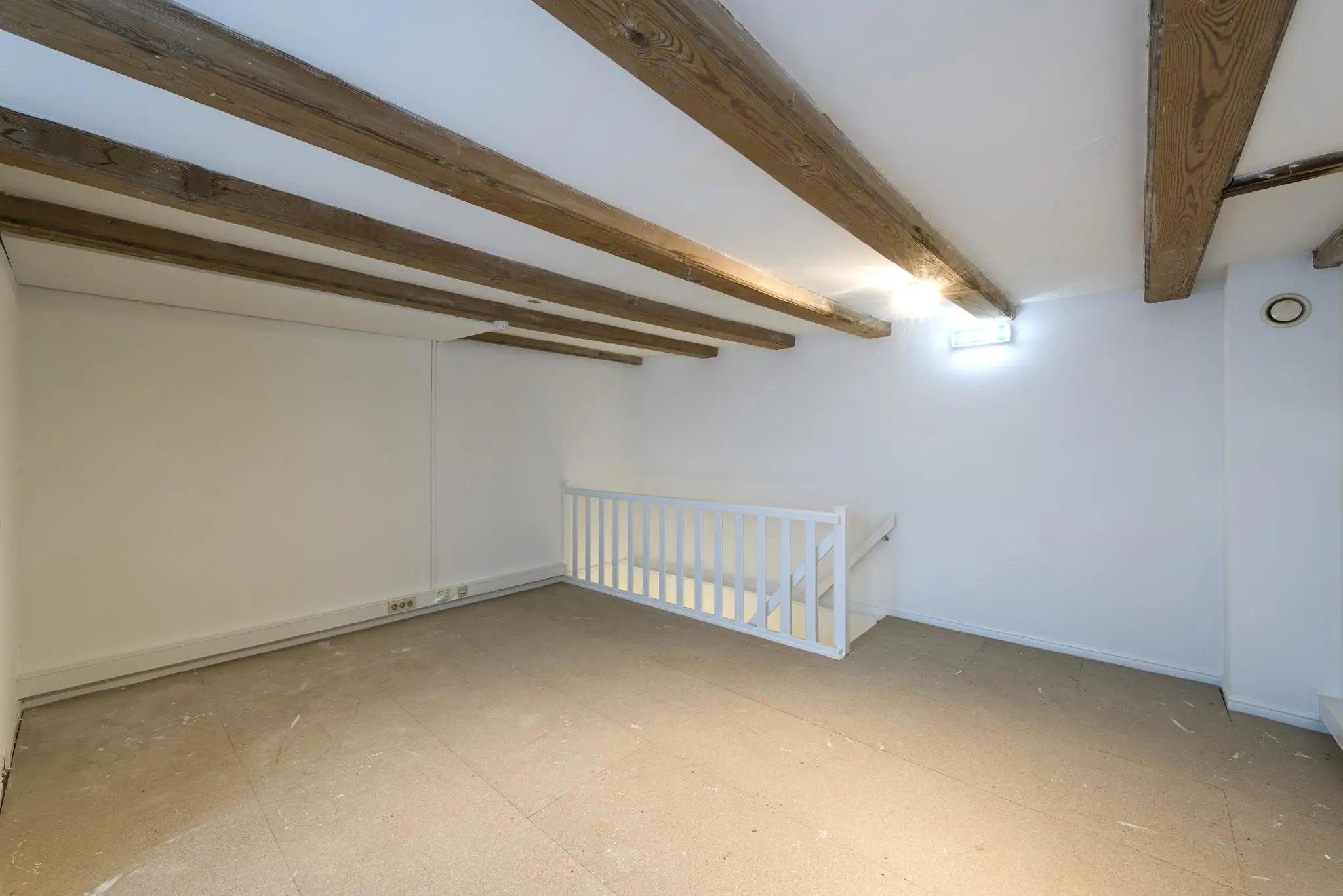 Zolderruimte aan de Herengracht met zichtbare houten plafondbalken, witte wanden en een trap met wit hekwerk.