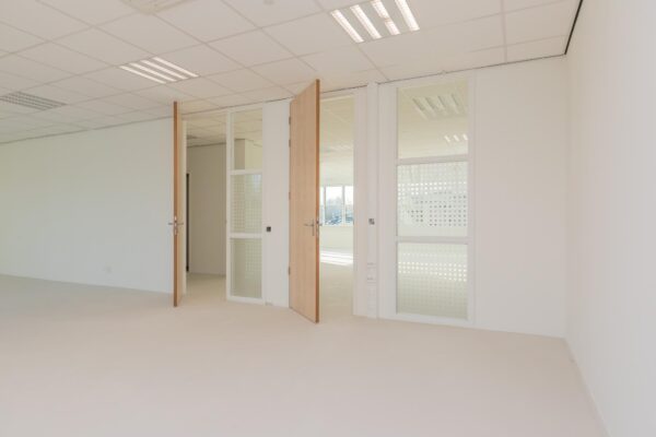 Lichte, lege kantoorruimte in het Rhijnspoor-gebouw met open houten deuren en glazen tussenwanden.