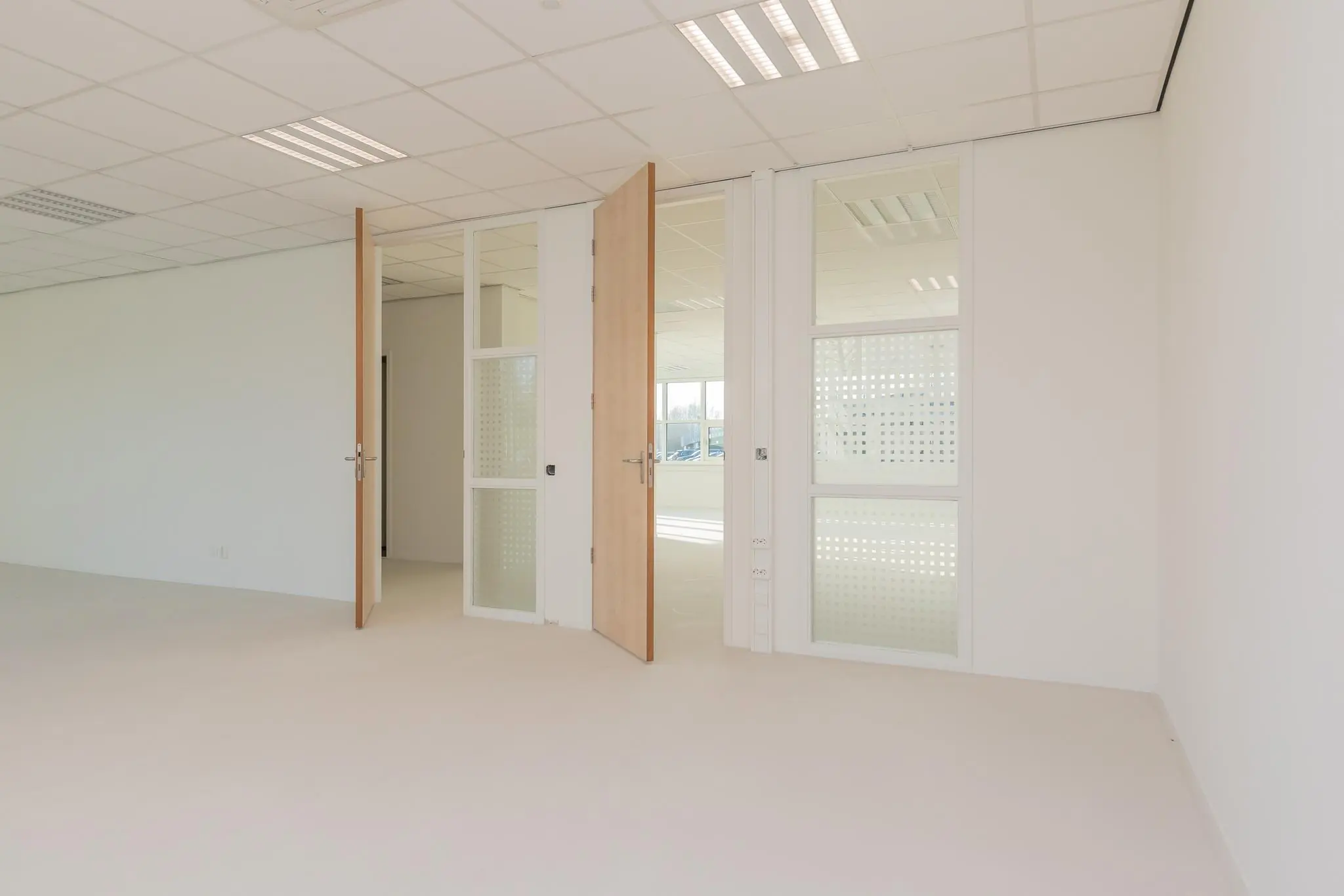 Lichte, lege kantoorruimte in het Rhijnspoor-gebouw met open houten deuren en glazen tussenwanden.
