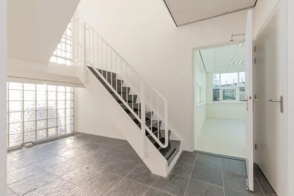 Lichte trappenhal met zwarte trap, glazen bouwstenen en een open deur naar een kantoorruimte in het gebouw Rhijnspoor.