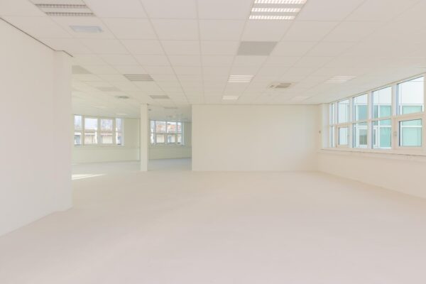 Lichte, lege kantoorruimte in het Rhijnspoor-gebouw met grote ramen en systeemplafond.
