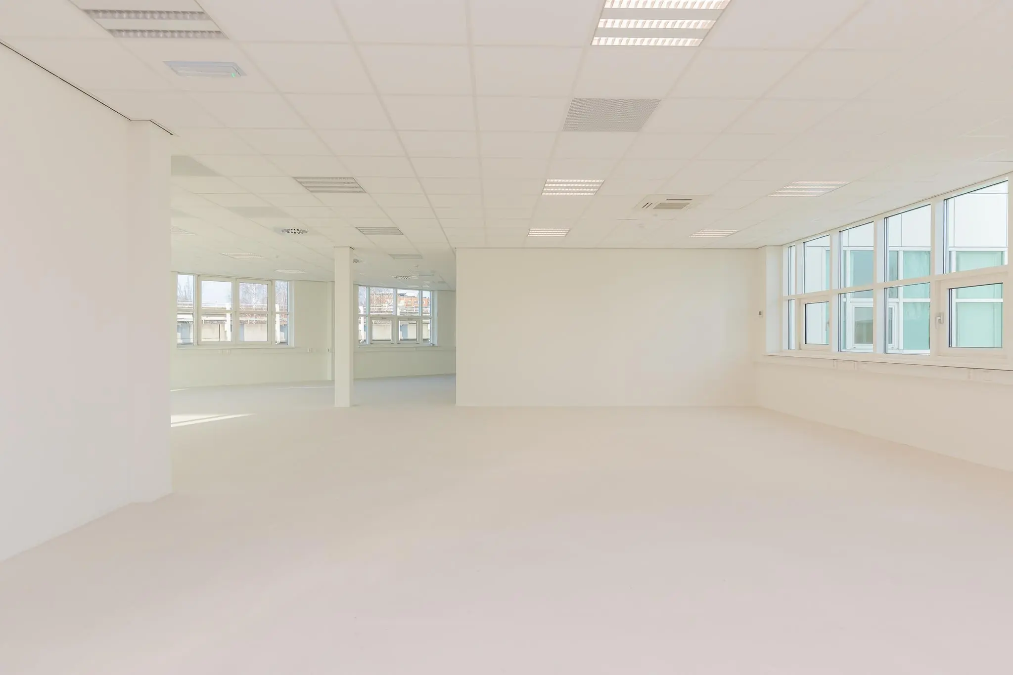 Lichte, lege kantoorruimte in het Rhijnspoor-gebouw met grote ramen en systeemplafond.