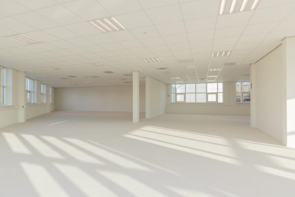 Lichte, lege kantoorruimte in het Rhijnspoor-gebouw met grote ramen en systeemplafond.