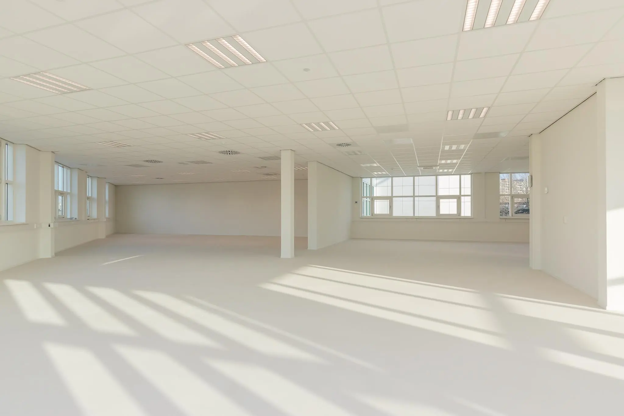 Lichte, lege kantoorruimte in het Rhijnspoor-gebouw met grote ramen en systeemplafond.