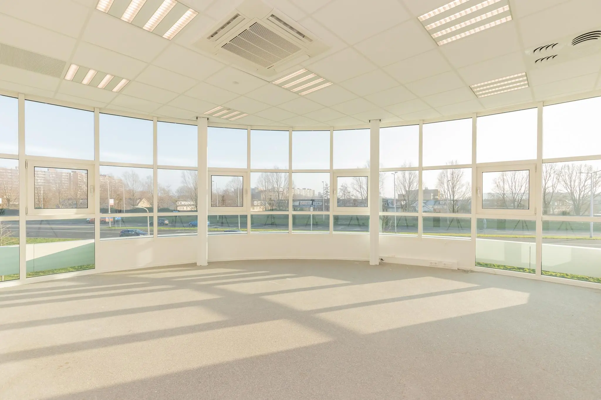 Lichte, lege kantoorruimte in Rhijnspoor met grote ramen en uitzicht op de weg en omliggende gebouwen.