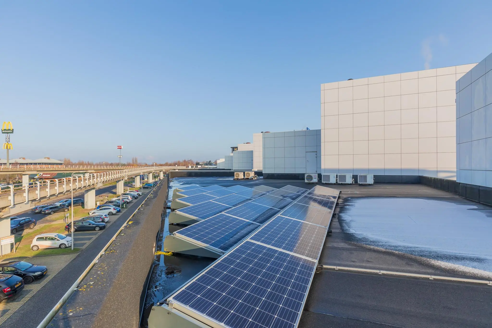 Zonnepanelen op het dak van een modern bedrijfsgebouw aan de Rhijnspoor in een stedelijke omgeving met parkeergelegenheid.