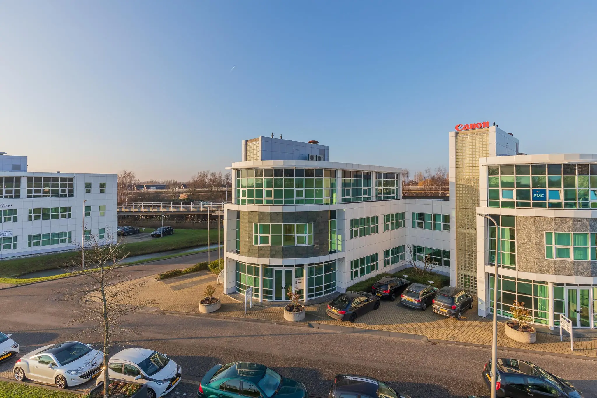 Kantoorpanden aan het Rhijnspoor met bedrijven zoals Canon en FMC, gezien op een zonnige dag.