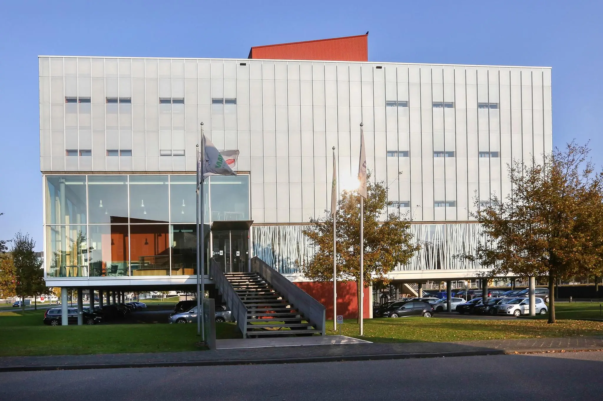 Modern kantoorgebouw aan de Hondiuslaan met glazen entree, vlaggen en parkeerplaatsen eronder.