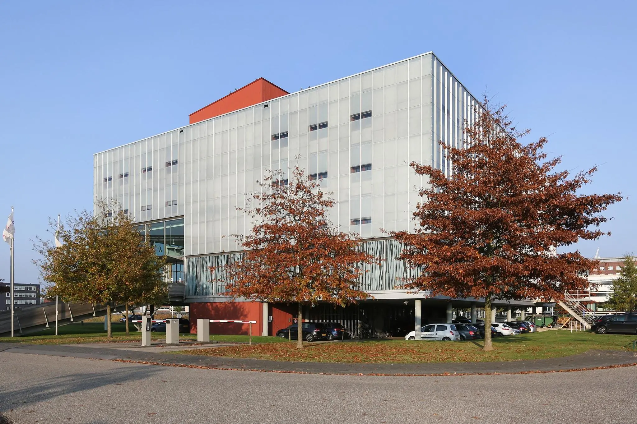 Modern kantoorgebouw aan de Hondiuslaan met bomen in herfstkleuren en geparkeerde auto's op de voorgrond.