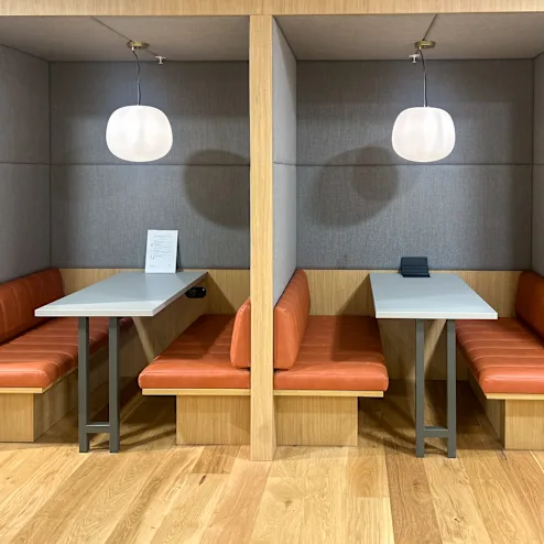 Twee moderne nissen met oranje banken en tafels, elk verlicht door een ronde hanglamp.