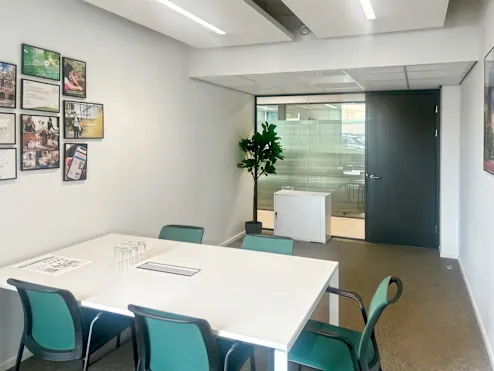 Een moderne vergaderruimte met een witte tafel, groene stoelen, en kunst aan de muur.