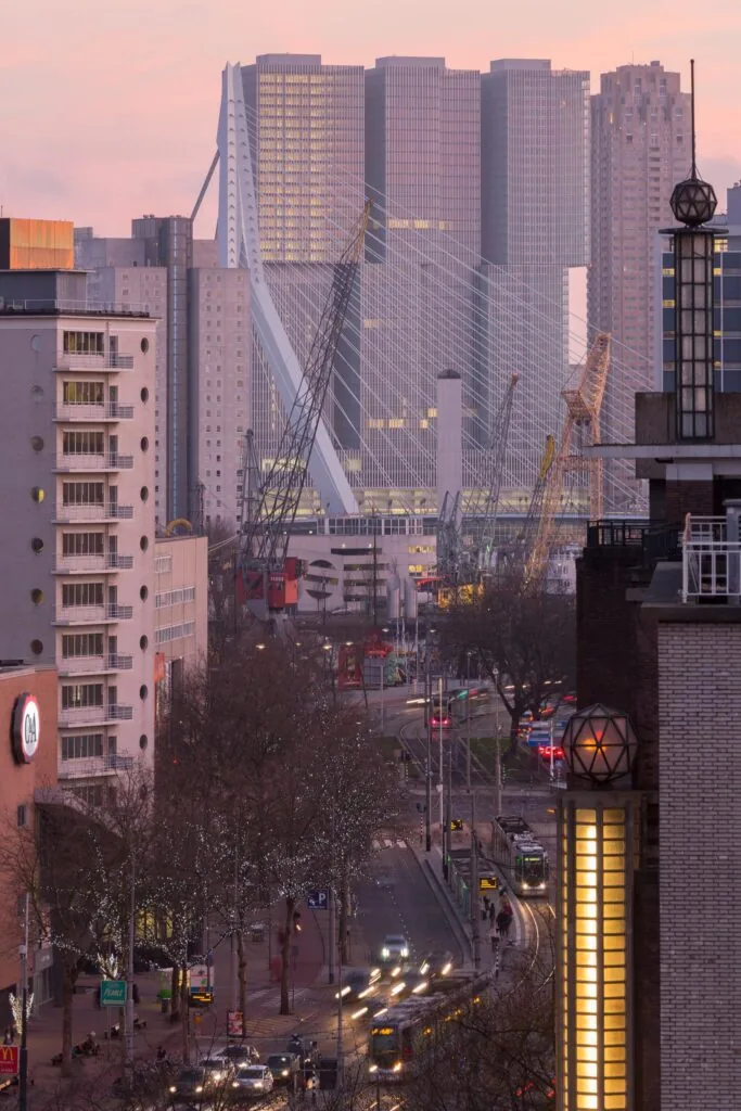 Uitzicht op de Wilhelminakade in Rotterdam met de Erasmusbrug en De Rotterdam op de achtergrond tijdens schemering.