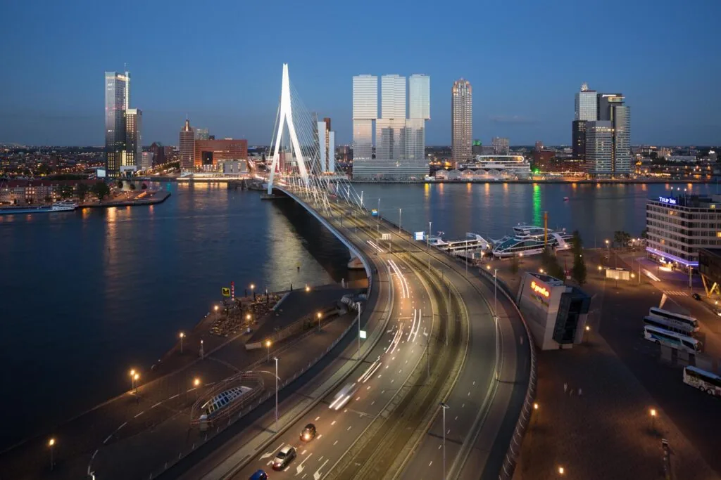 Avondzicht op de Wilhelminakade in Rotterdam met de verlichte Erasmusbrug en moderne hoogbouw op de achtergrond.
