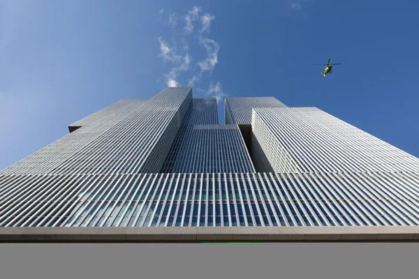 Modern hoogbouwcomplex De Rotterdam aan de Wilhelminakade met een gele helikopter in de lucht erboven.