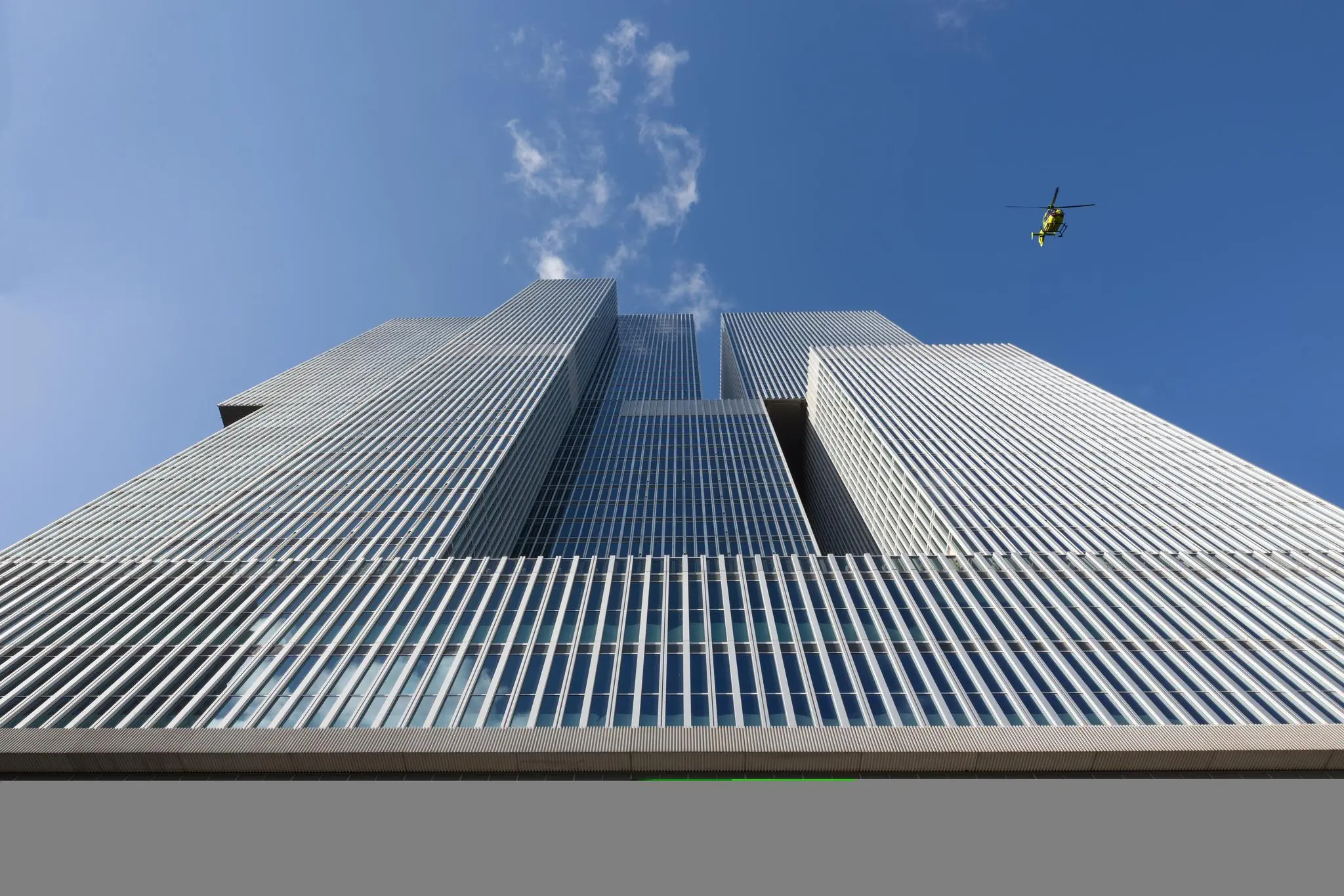 Modern hoogbouwcomplex De Rotterdam aan de Wilhelminakade met een gele helikopter in de lucht erboven.