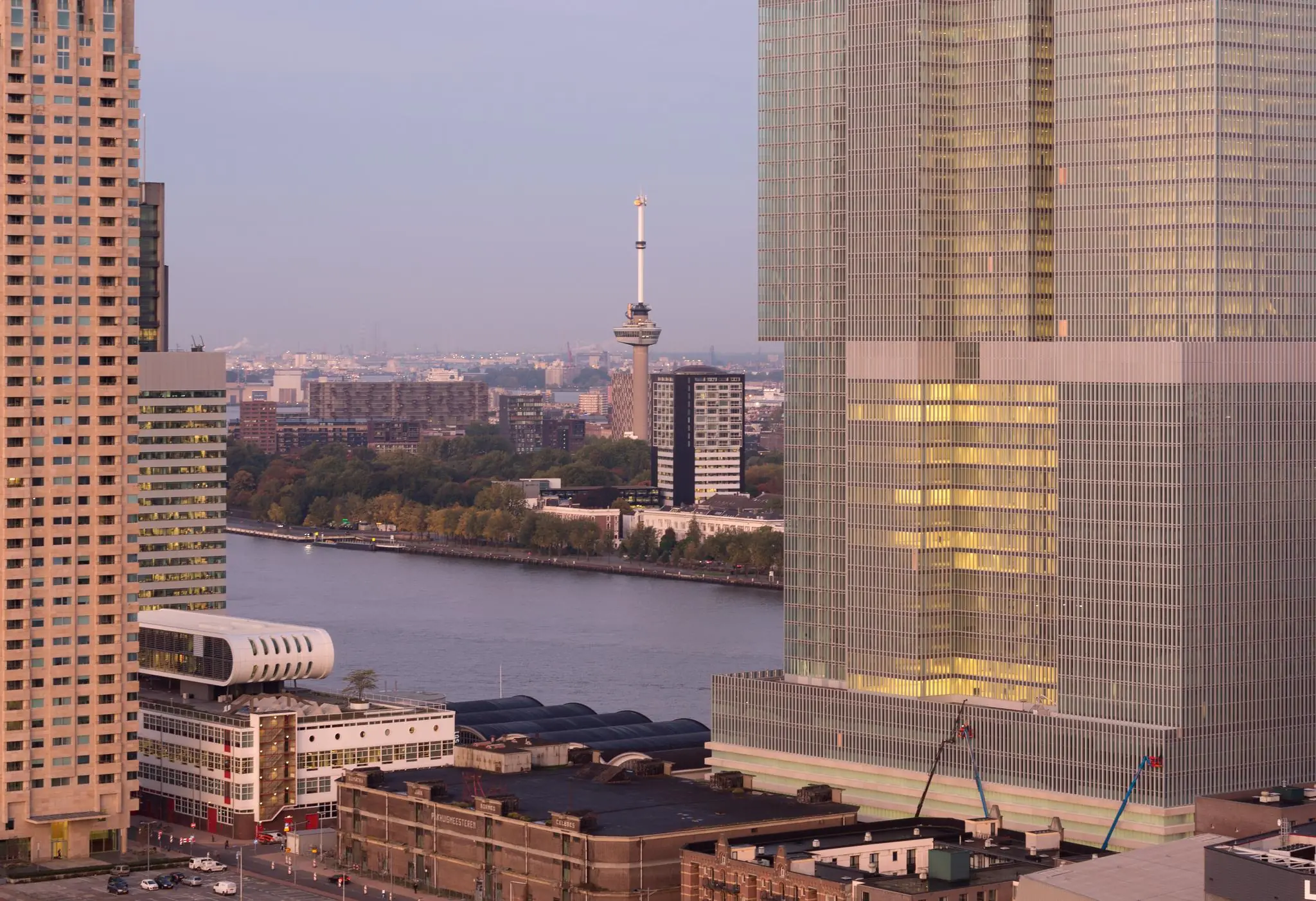 Uitzicht op de Wilhelminakade in Rotterdam met moderne hoogbouw, de Euromast en de Maas op de achtergrond.