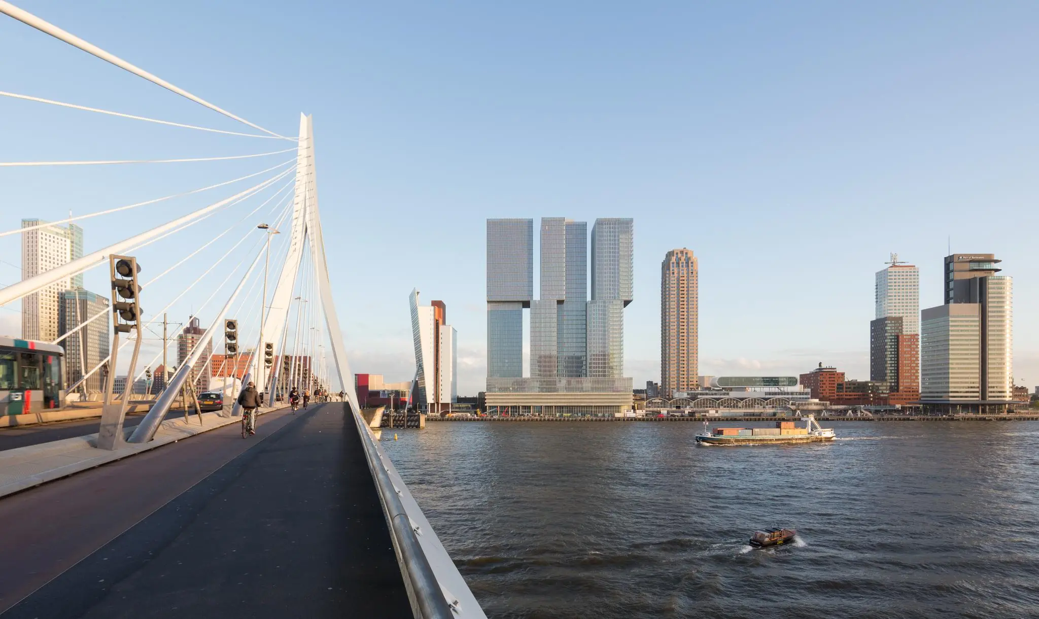 Uitzicht vanaf de Erasmusbrug op de Wilhelminakade in Rotterdam met moderne hoogbouw en varende schepen op de Maas.