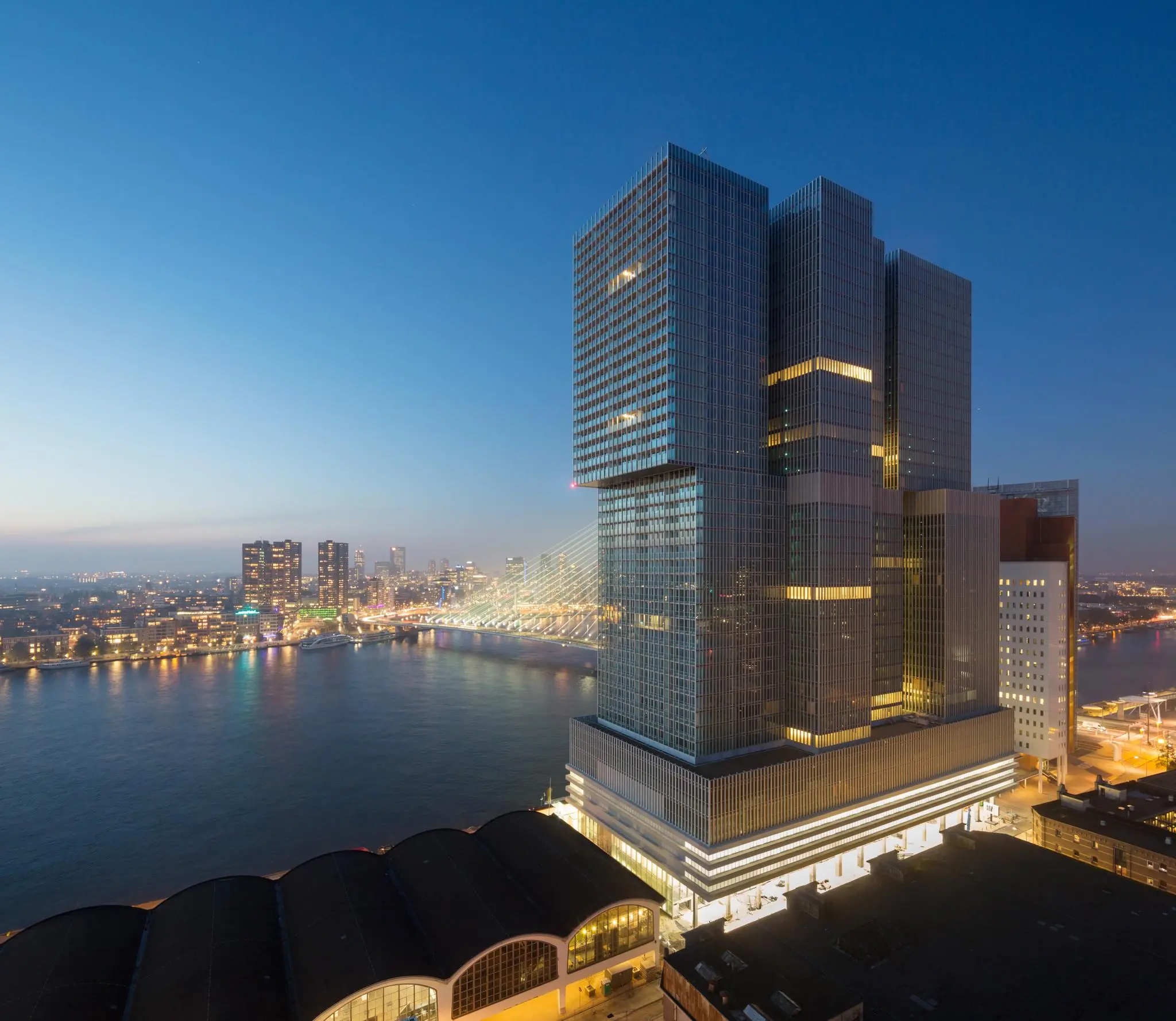 De Rotterdam met uitzicht op de Erasmusbrug bij avondlicht vanaf de Wilhelminakade in Rotterdam.