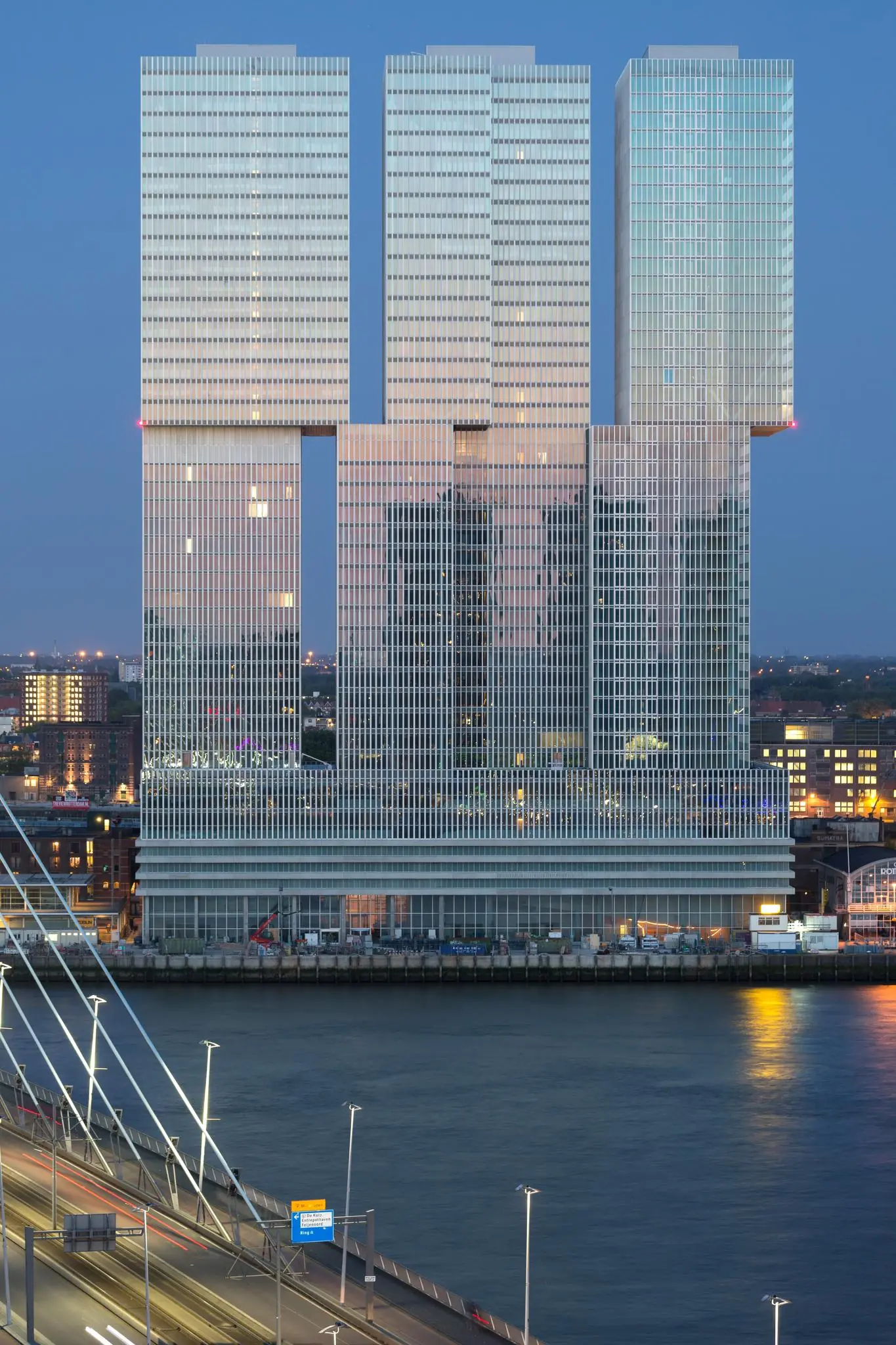 Modern hoogbouwcomplex De Rotterdam aan de Wilhelminakade in Rotterdam, gefotografeerd bij schemering vanaf de overzijde van de Maas.