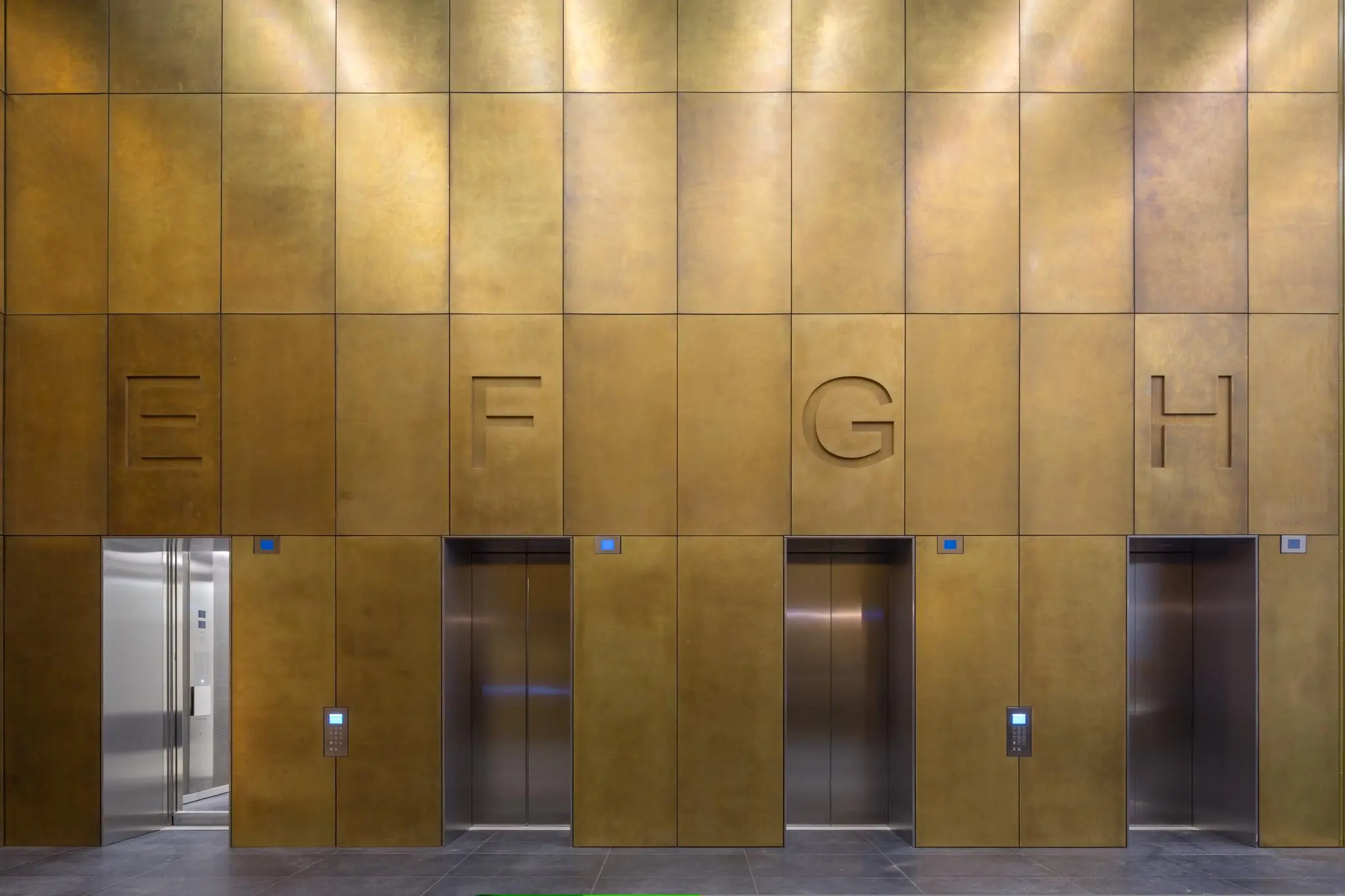 Vier liften met de letters E, F, G en H in een gouden wand aan de Wilhelminakade.