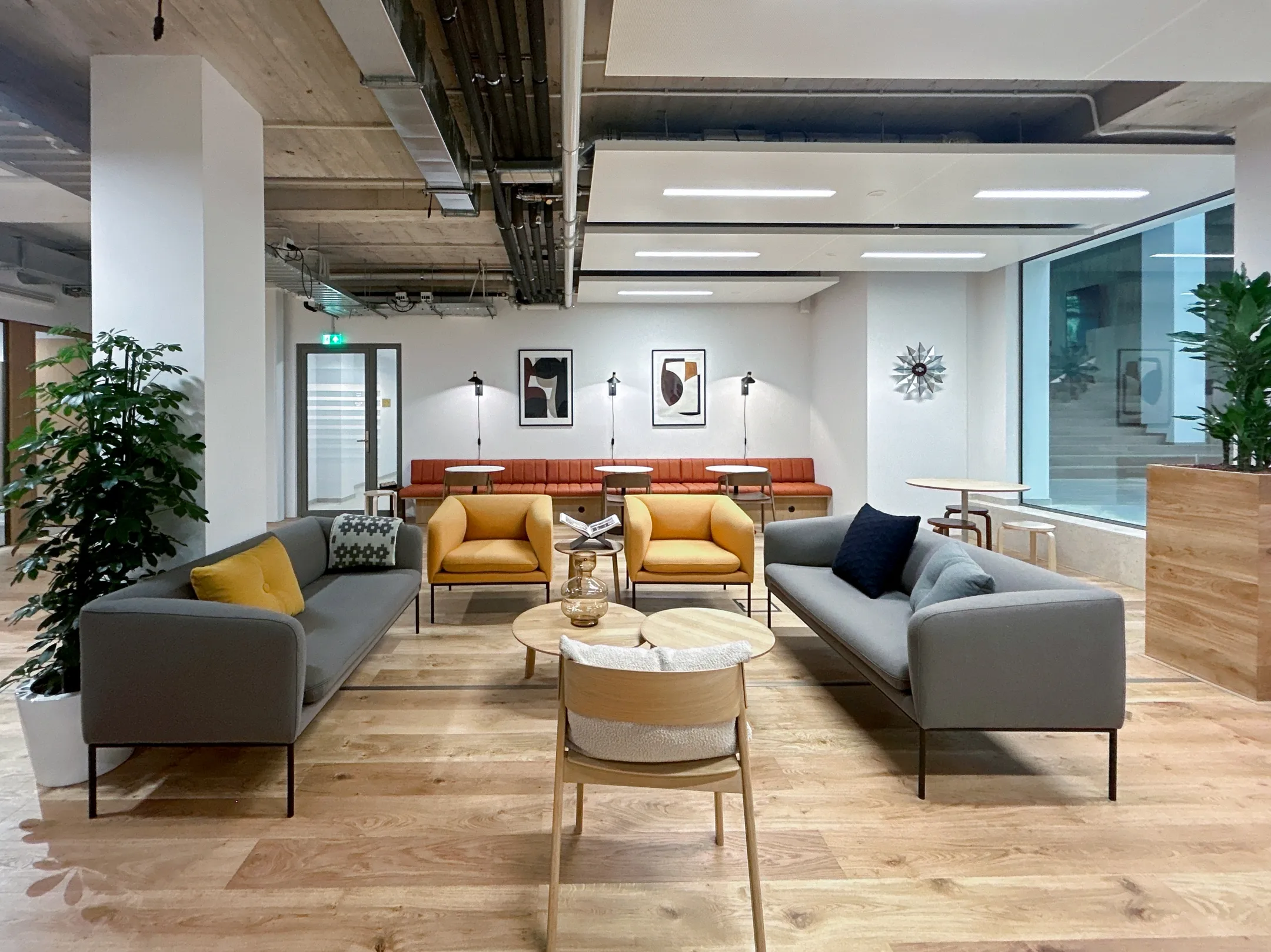 Moderne, uitnodigende lounge met grijze en gele zitmeubels, houten tafels en planten.