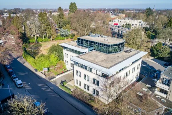 Luchtfoto van een modern kantoorgebouw aan de Amalialaan, omgeven door bomen en woonhuizen.