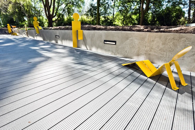 Moderne buitenruimte aan de Vlaardingenlaan met gele stalen figuren tegen een betonnen muur en houten vlonder.