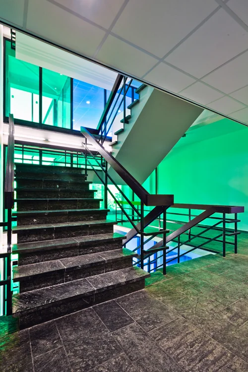 Trapportaal in modern kantoorgebouw aan de Vlaardingenlaan met zwarte stenen treden en groene verlichting.