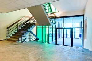 Ingangshal van een modern gebouw aan de Vlaardingenlaan met trap en grote ramen met gekleurde glaspartijen.