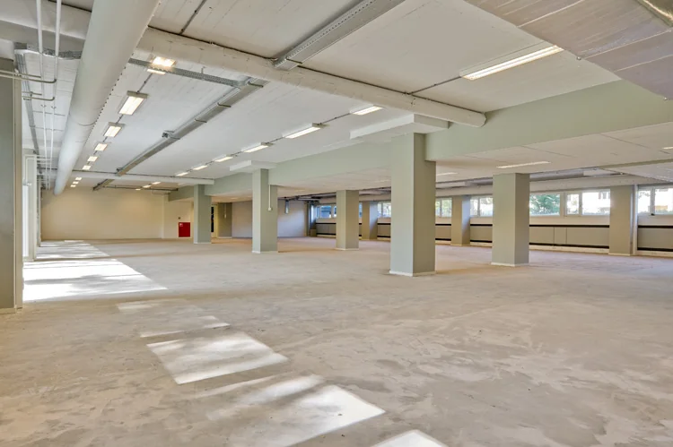 Lichte, lege kantoorruimte aan de Vlaardingenlaan met betonnen vloer en zichtbare plafondinstallaties.
