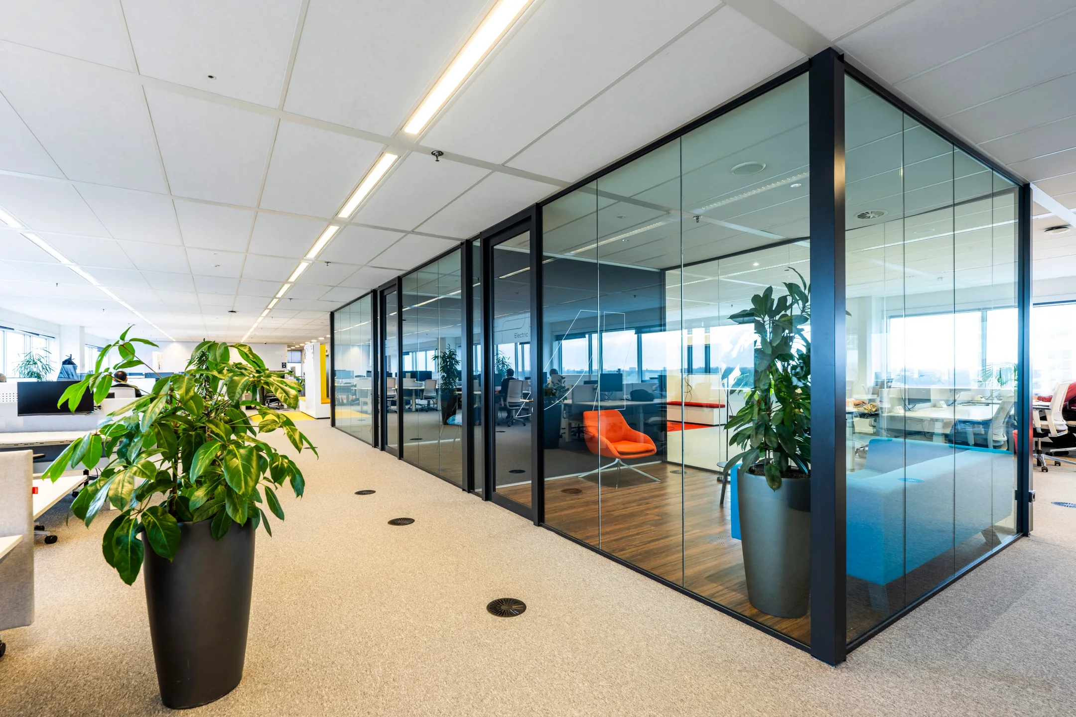 Een moderne kantoorruimte met glazen wanden, planten en een feloranje stoel.