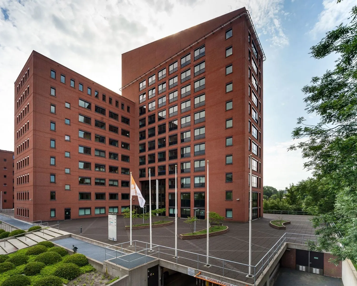 Roodbruin kantoorgebouw met meerdere verdiepingen en vlaggenmasten op het voorplein.