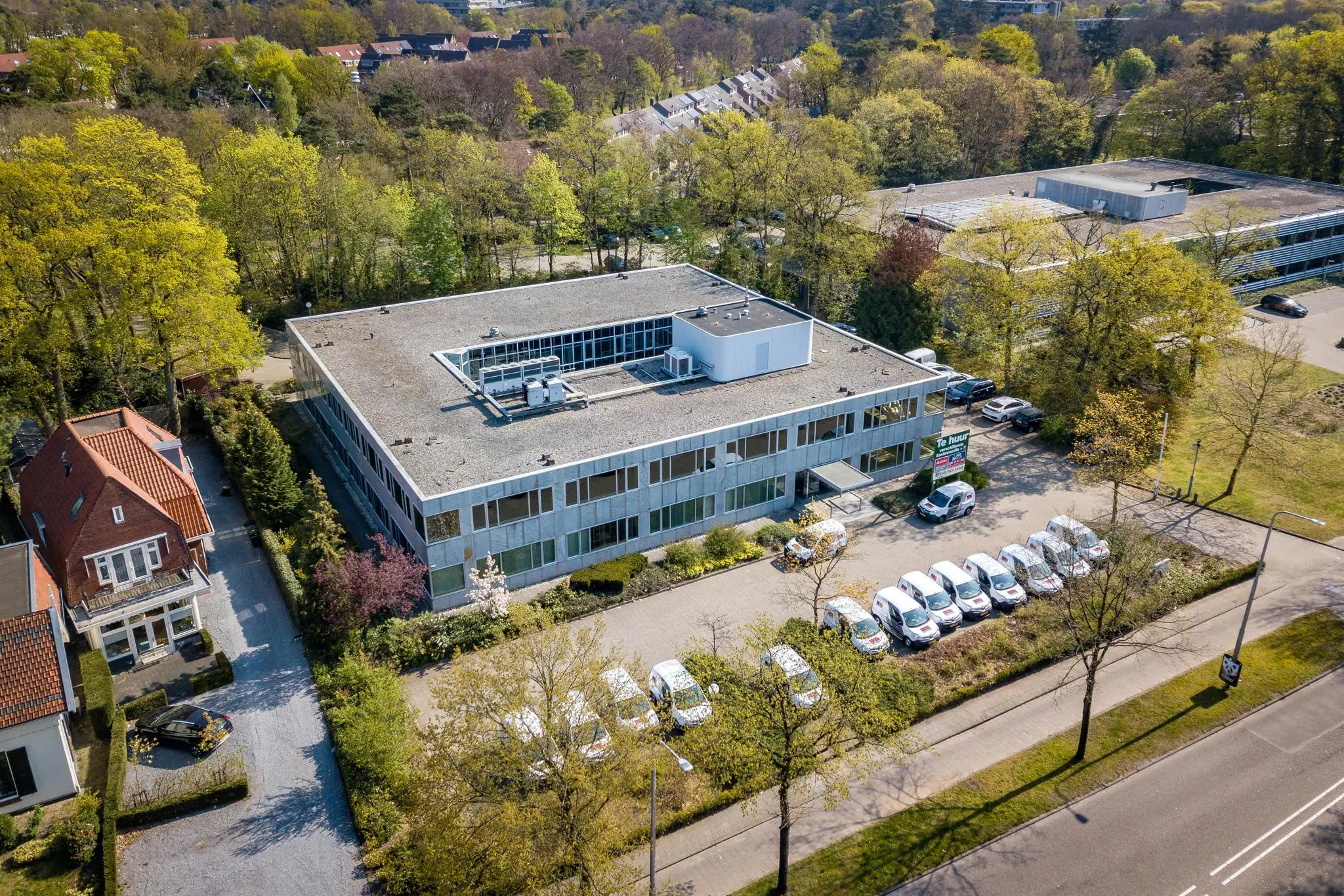 Luchtfoto van een kantoorpand aan de Utrechtseweg met parkeerplaatsen en omringende bomen.