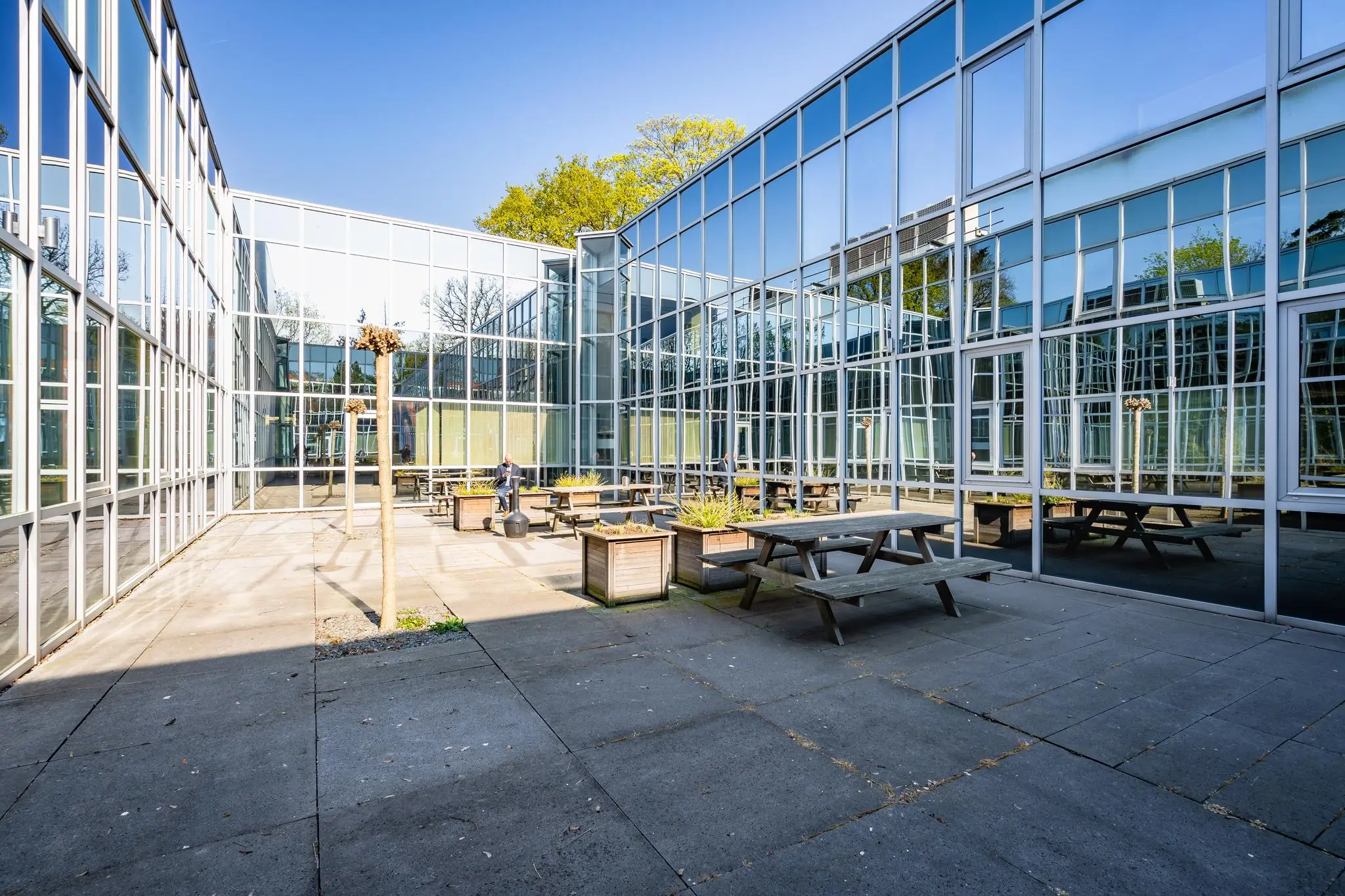 Binnenplaats met picknicktafels en plantenbakken tussen glazen gevels van een modern kantoorgebouw aan de Utrechtseweg.