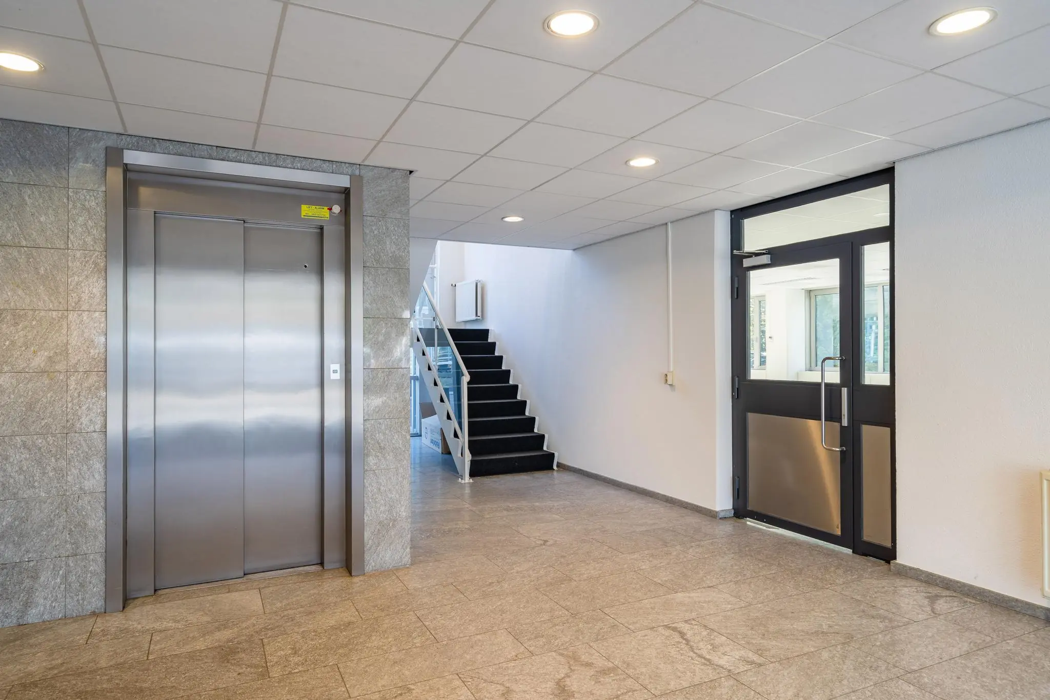 Ingangshal van een kantoorpand aan de Utrechtseweg met een lift, trap en glazen deur.